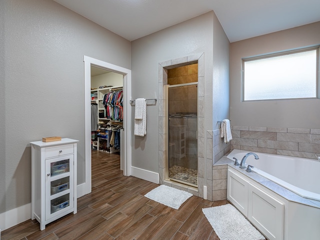 full bath with wood finished floors, a bath, a stall shower, and a walk in closet