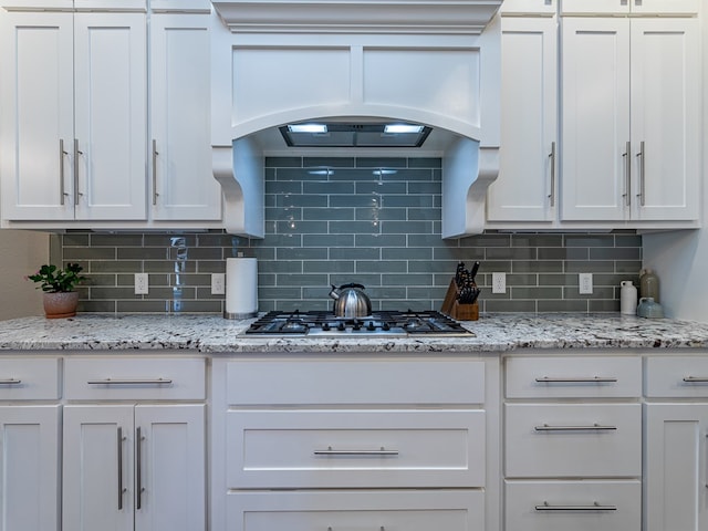 kitchen with stainless steel gas stovetop, decorative backsplash, white cabinets, and custom range hood
