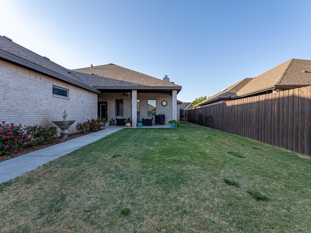 back of property with a patio, outdoor lounge area, a shingled roof, a yard, and a fenced backyard
