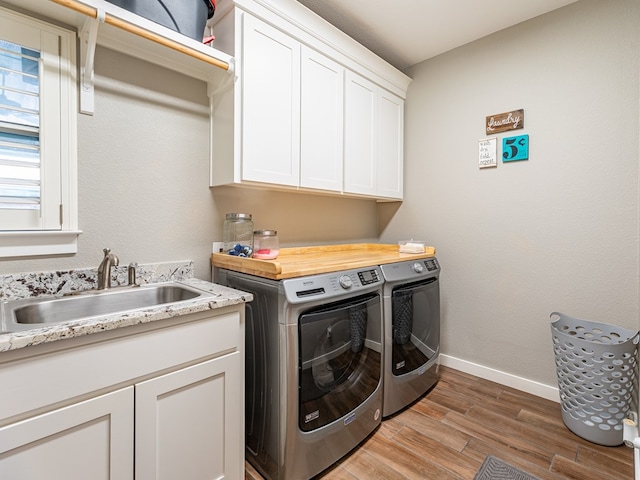 clothes washing area featuring a sink, baseboards, washer and dryer, cabinet space, and wood finished floors