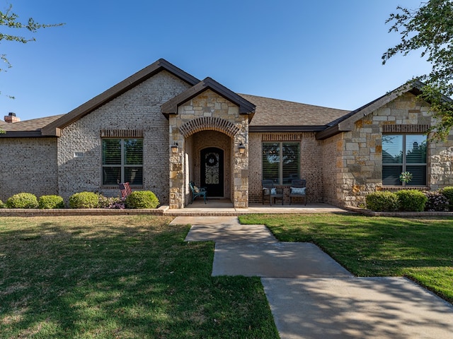 view of front of house with brick siding, a shingled roof, a front yard, and stone siding