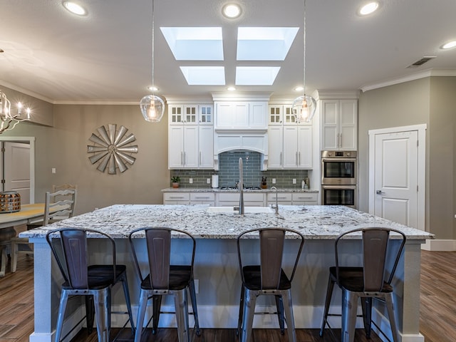 kitchen featuring stainless steel double oven, ornamental molding, a large island, backsplash, and dark wood-style floors