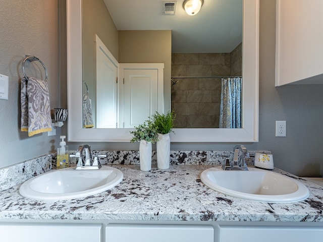 bathroom featuring visible vents, a tile shower, double vanity, and a sink