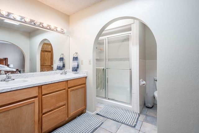 bathroom with tile patterned flooring, an enclosed shower, vanity, a textured ceiling, and toilet