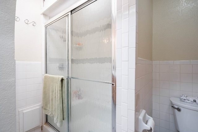 bathroom featuring a shower with door, tile walls, and toilet