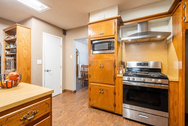 kitchen with wall chimney range hood, light hardwood / wood-style flooring, stainless steel appliances, and a textured ceiling