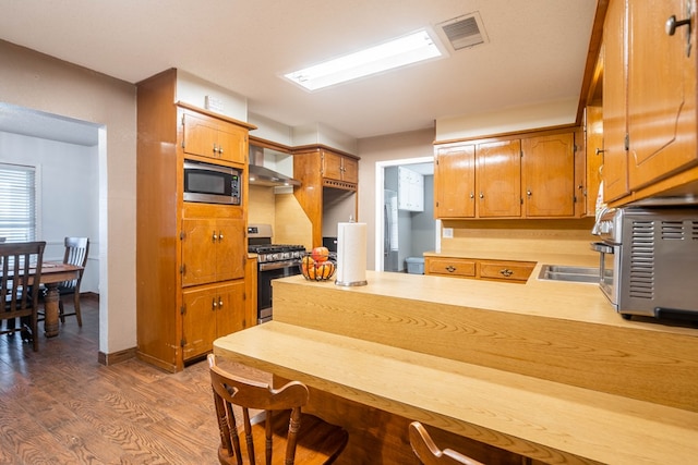 kitchen with sink, dark wood-type flooring, appliances with stainless steel finishes, kitchen peninsula, and wall chimney exhaust hood