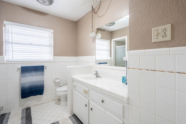 bathroom with tile walls, vanity, a textured ceiling, tile patterned floors, and toilet