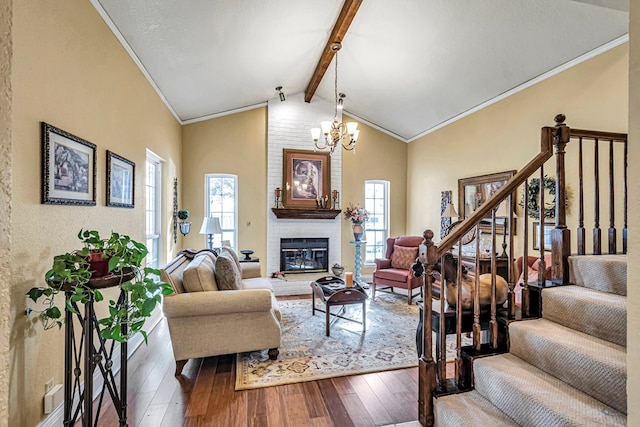 living room featuring an inviting chandelier, hardwood / wood-style flooring, a brick fireplace, crown molding, and lofted ceiling with beams