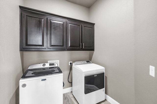 washroom featuring cabinet space, washing machine and clothes dryer, light wood-style flooring, and baseboards