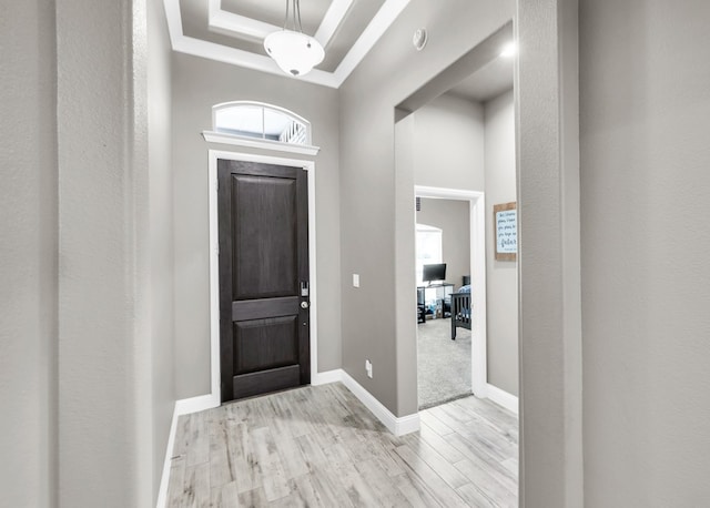 foyer with a tray ceiling, wood finished floors, ornamental molding, and baseboards