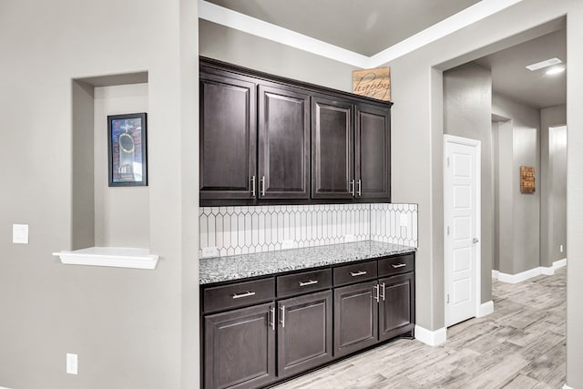 kitchen with backsplash, light wood-type flooring, light stone countertops, dark brown cabinets, and baseboards