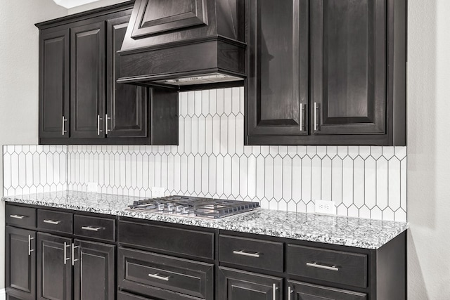 kitchen featuring backsplash, stainless steel gas cooktop, custom exhaust hood, and light stone countertops