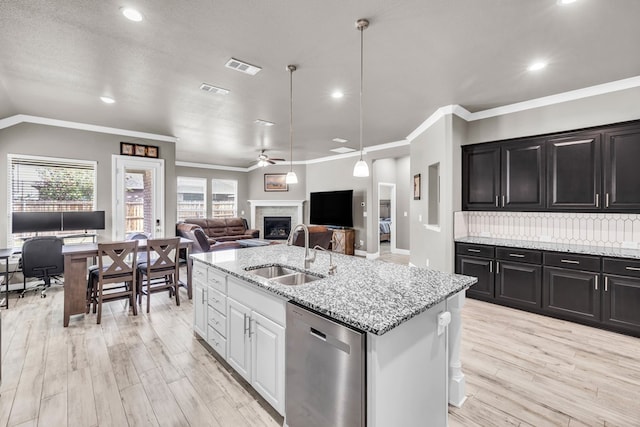 kitchen with a sink, dishwasher, a fireplace, a ceiling fan, and a kitchen island with sink