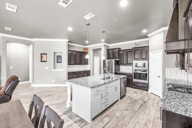 kitchen with stainless steel appliances, recessed lighting, premium range hood, light wood-style floors, and an island with sink