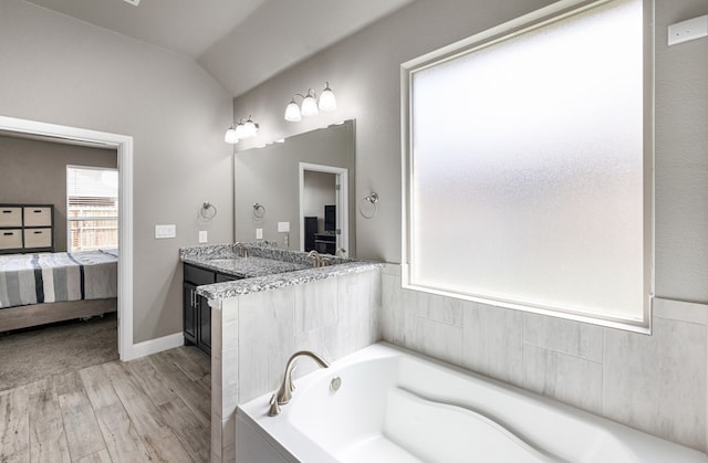 full bathroom with ensuite bath, wood finished floors, a bath, vanity, and lofted ceiling