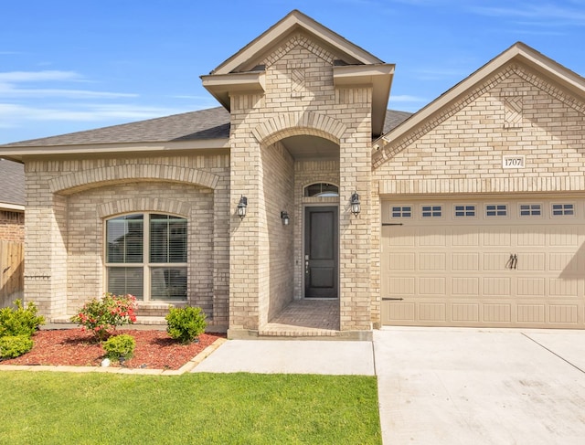 french provincial home with brick siding, a garage, driveway, and roof with shingles