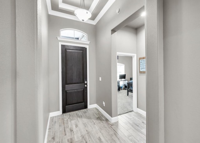 entryway with a raised ceiling, wood finished floors, crown molding, and baseboards