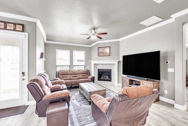 living room featuring ceiling fan, crown molding, baseboards, light wood-style floors, and a glass covered fireplace