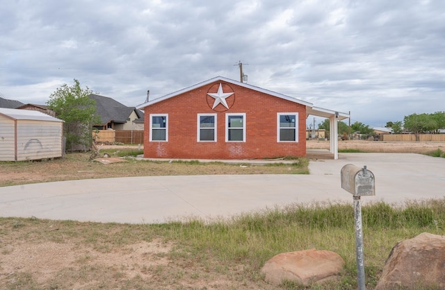 view of side of property featuring concrete driveway, brick siding, fence, and a carport