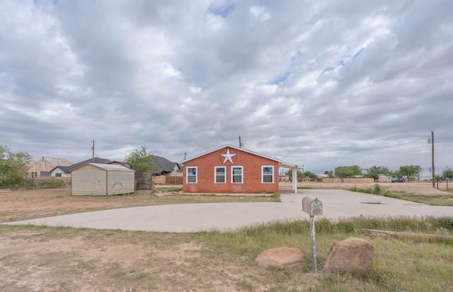 view of front of property featuring concrete driveway, a storage shed, an outbuilding, and brick siding