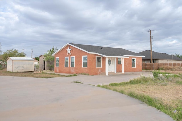 view of front of home featuring fence, brick siding, concrete driveway, an outdoor structure, and a shed