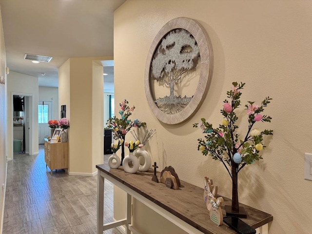 hall with wood finished floors, visible vents, and baseboards