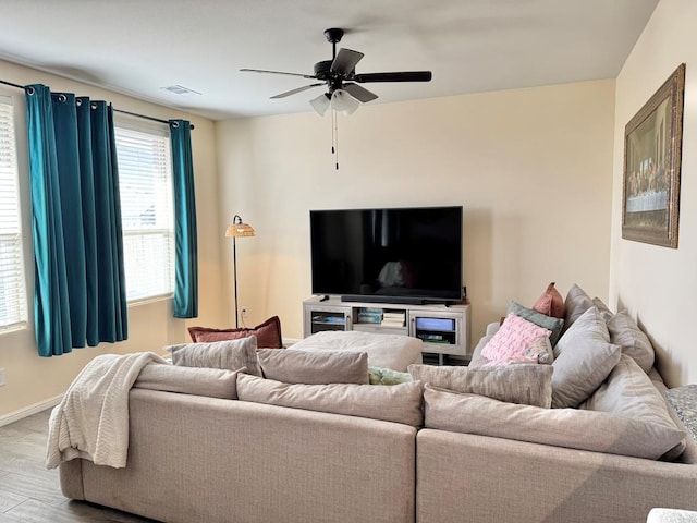 living room featuring ceiling fan, light wood-type flooring, visible vents, and baseboards