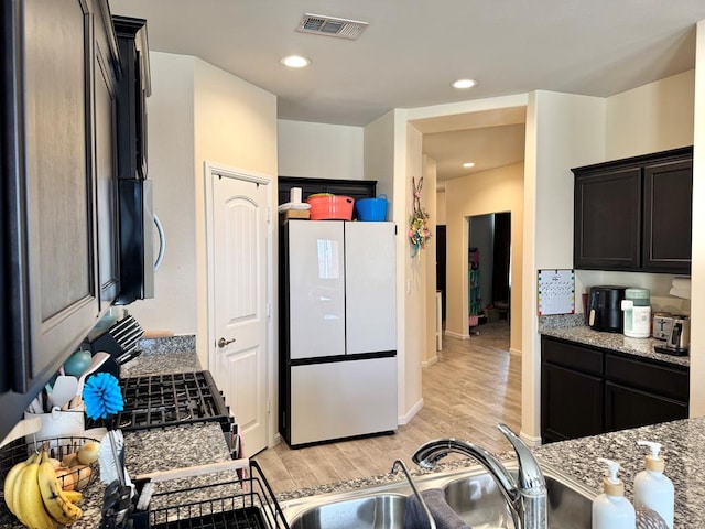 kitchen featuring light stone counters, freestanding refrigerator, visible vents, and light wood finished floors