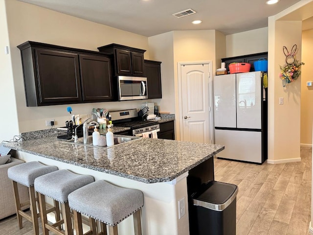 kitchen with stainless steel appliances, visible vents, a sink, light wood-type flooring, and a peninsula