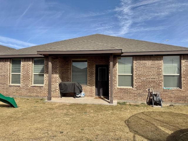 back of property featuring a yard, brick siding, roof with shingles, and a patio area