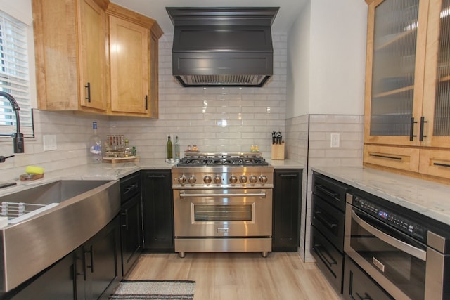 kitchen featuring stainless steel range, light stone countertops, custom range hood, and light wood-type flooring