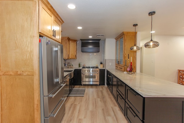 kitchen featuring high end appliances, light wood-type flooring, kitchen peninsula, pendant lighting, and wall chimney range hood