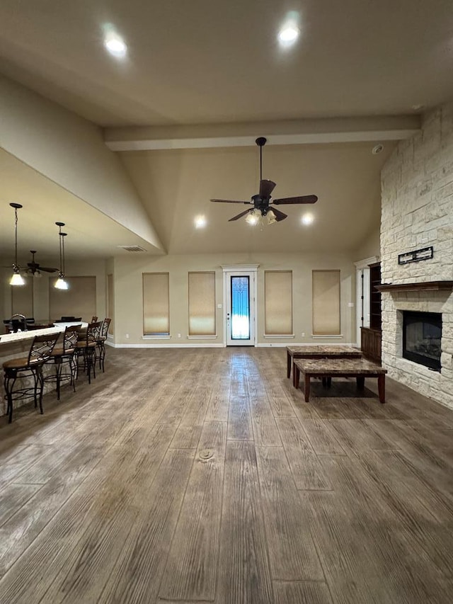 living room with a stone fireplace, wood-type flooring, beamed ceiling, and ceiling fan