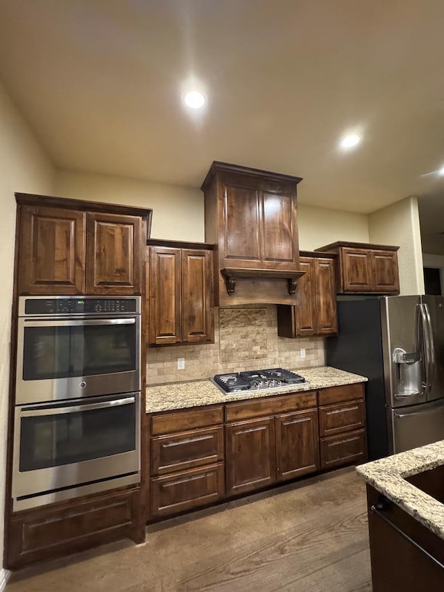 kitchen with tasteful backsplash, dark hardwood / wood-style flooring, dark brown cabinetry, light stone counters, and stainless steel appliances