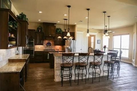 kitchen with appliances with stainless steel finishes, a kitchen bar, hanging light fixtures, and a large island with sink