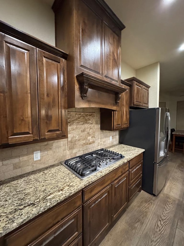 kitchen with dark brown cabinets, light wood-type flooring, stainless steel appliances, light stone countertops, and decorative backsplash