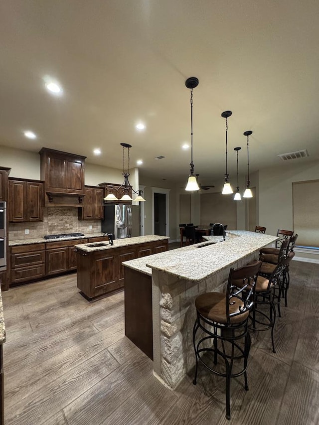 kitchen with tasteful backsplash, decorative light fixtures, dark brown cabinets, a large island with sink, and a kitchen breakfast bar