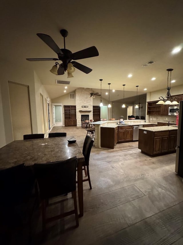 kitchen with dark brown cabinetry, sink, hanging light fixtures, appliances with stainless steel finishes, and a kitchen island with sink