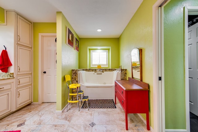 bathroom with a tub with jets, a textured wall, and baseboards