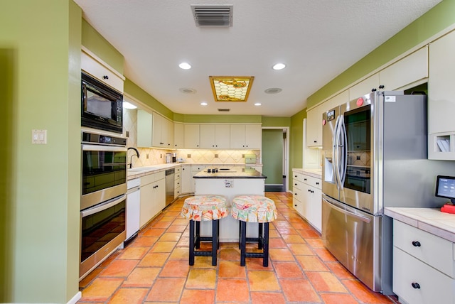 kitchen with visible vents, white cabinetry, decorative backsplash, a kitchen island, and stainless steel appliances