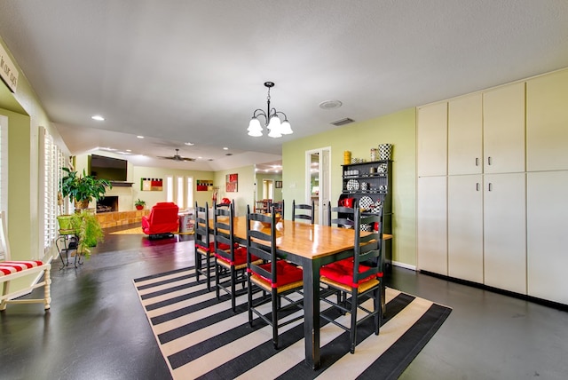 dining area with concrete flooring, a fireplace, ceiling fan with notable chandelier, and recessed lighting