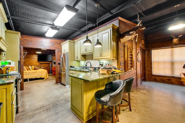 kitchen featuring pendant lighting, a breakfast bar, wood walls, and stainless steel refrigerator