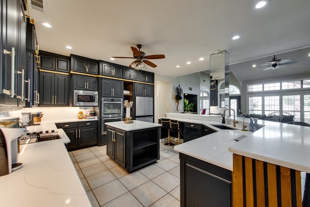 kitchen with light stone counters, stainless steel appliances, ceiling fan, sink, and a kitchen island