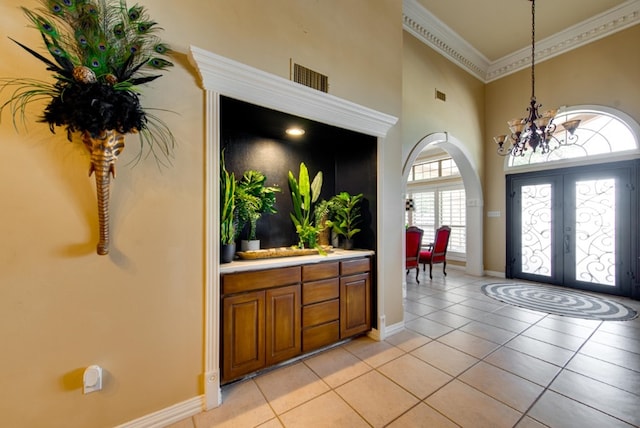 tiled foyer featuring a chandelier, french doors, a towering ceiling, and ornamental molding