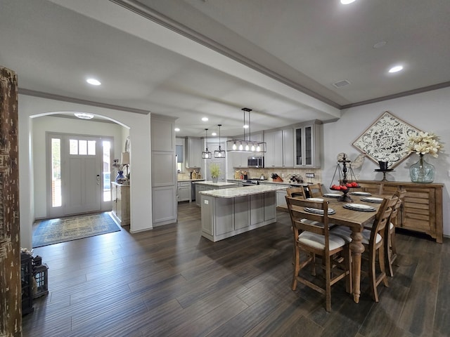 kitchen with a center island, decorative light fixtures, light stone counters, dark wood-type flooring, and crown molding