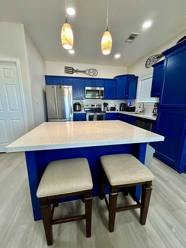 kitchen with blue cabinetry, light hardwood / wood-style flooring, decorative light fixtures, and appliances with stainless steel finishes