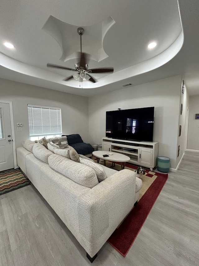 living room featuring a tray ceiling, ceiling fan, and light hardwood / wood-style floors