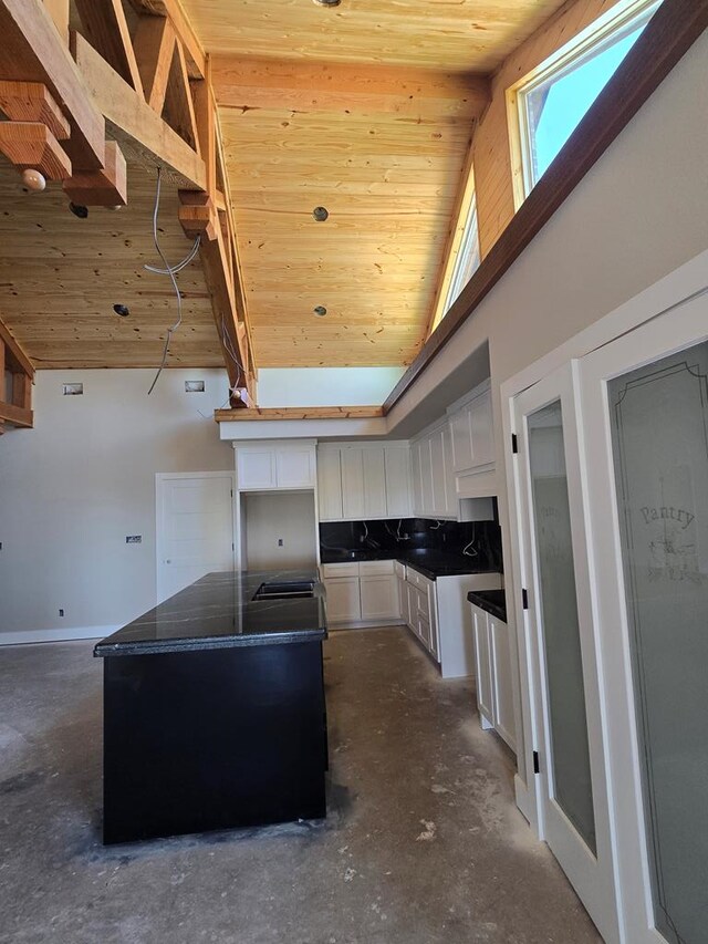 kitchen with a center island, wooden ceiling, high vaulted ceiling, dark stone countertops, and white cabinets