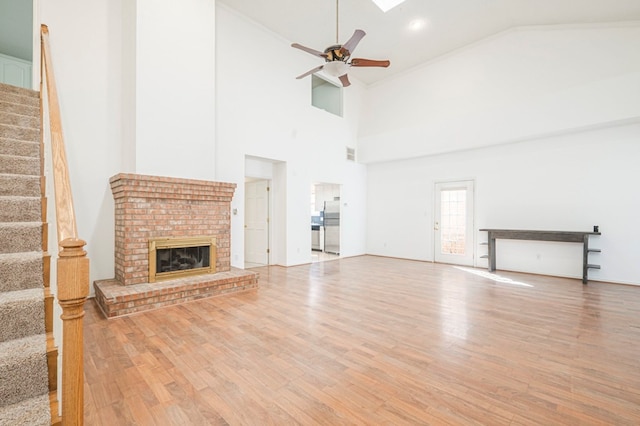 unfurnished living room with ceiling fan, wood finished floors, visible vents, stairs, and a brick fireplace